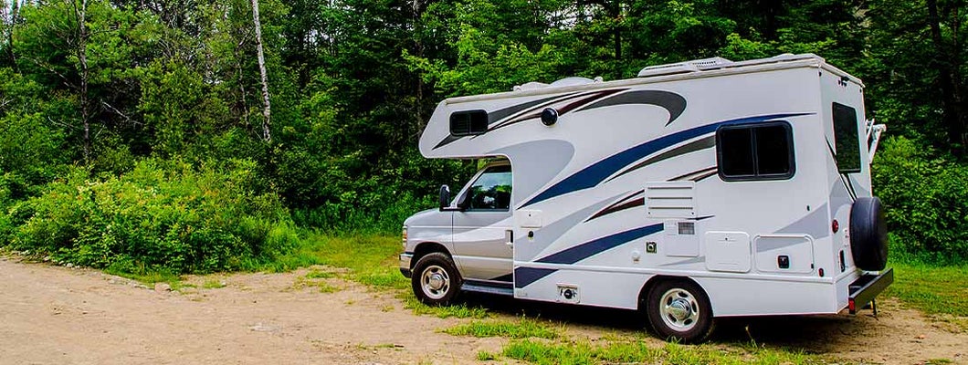 RV parked on sand in forest during day of summer. Find Delaware RV Insurance. 