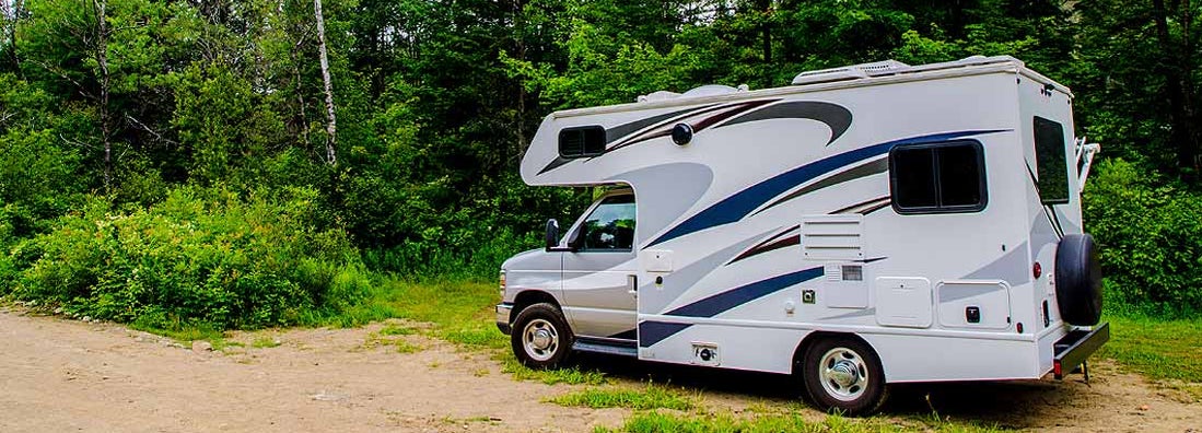 RV parked on sand in forest during day of summer. Find Delaware RV Insurance. 