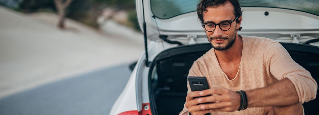 Young man sitting on car trunk. Find El Paso Texas car insurance.