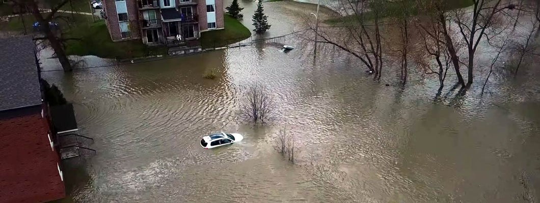 Aerial view of floods affecting a white car and two houses and several trees and branches. Find Utah flood insurance.