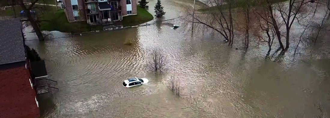 Aerial view of floods affecting a white car and two houses and several trees and branches. Find Utah flood insurance.