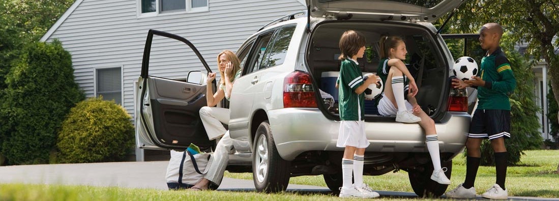 Kids with soccer balls by car in driveway. Umbrella Insurance Discounts.