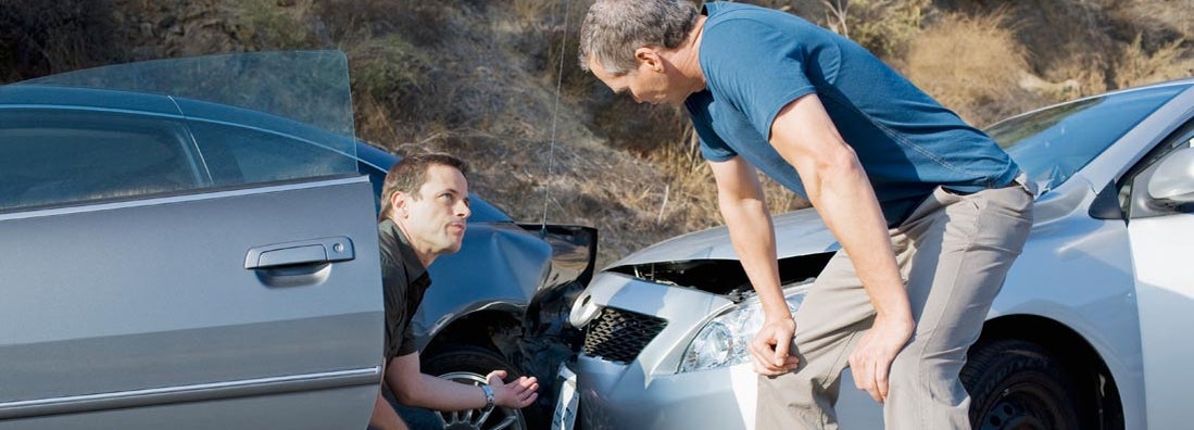 Two men examining damage in car collision. Who's responsible for damages if both drivers were at fault?