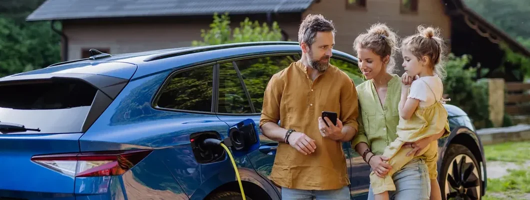 Family standing in front of their house with solar panels on the roof and an electric car. Find Home Insurance Bundles.