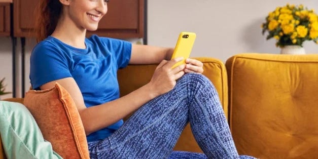 Une femme est assise sur un canapé et regarde son téléphone.