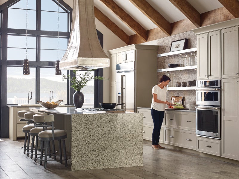 A woman cooking in a large open kitchen with a marble island and wood kitchen cabinets.
