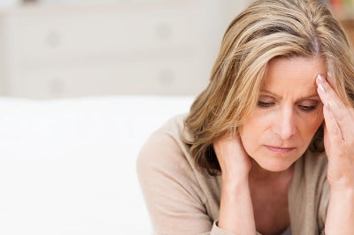 A woman with blonde hair holds her forehead as if worried.