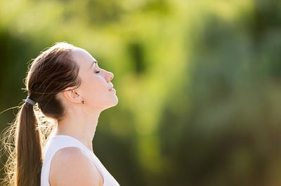 A young woman with her eyes closed raising her head toward the sky as if taking in a breathe of fresh air.
