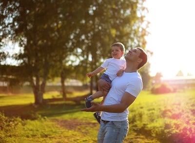 A man holds his young son while looking up at the sun.