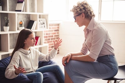 A teenage girl expressing with her hands held wide while talking to an adult female counselor.