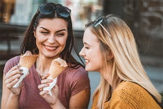 Two young women sit smiling eating ice cream cones.