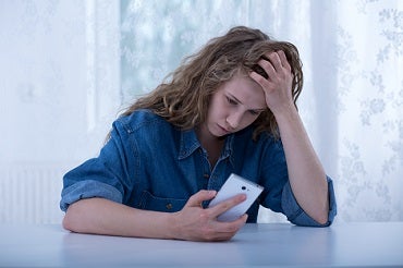 Young woman holding her head looking at her cell phone.
