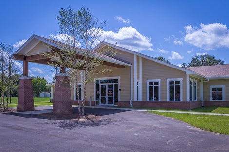 Tan building with white trim to include double front doors with a large overhead cover for drop offs.