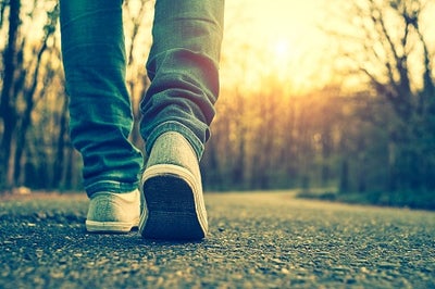 Someone's feet wearing sneakers while walking on pavement toward the sunrise.