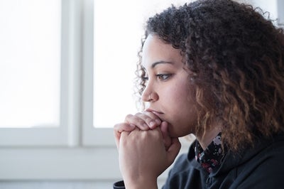 Young woman, perhaps a victim of trauma, sits in reflection with her chin resting in her hands clasped while she stairs ahead.
