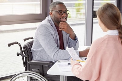 Man in wheelchair meeting with lady discussing notes.