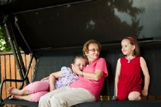 A woman of about 60 to 70 years old smiles at two young girls probably her granddaughters while sitting on a swing.