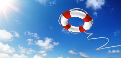 A read and white life preserver is flying above in the bright blue sky as if it's been tossed by someone and the sun is shining to the left.