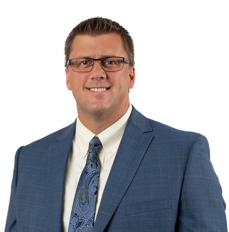A close up a of man smiling at the camera with short hair and glasses wearing a blue suit and tie.