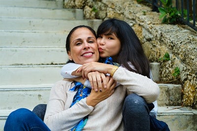 Hispanic young woman hugging an older women of similar ethnicity while sitting on steps. 