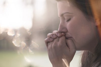 Young lady holding hands together up to mouth with closed eyes thinking.