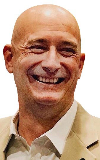 Man with bald head and tan jacket smiles.