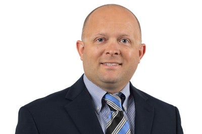 Mand in blue suit with tie smiling at camera.