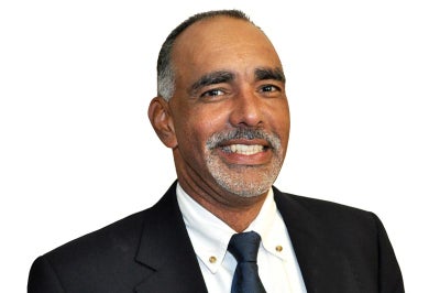 Man with brown skin and graying hair wearing a tie smiles at camera.