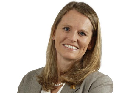 Professional young woman wearing pearls and a tan jacket smiles at camera.