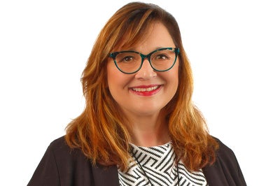Woman with red hair, glasses and a black jackets smiles at camera.