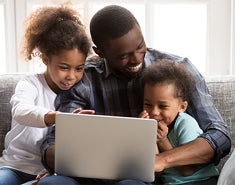 A black father laughs with two children on laptop.