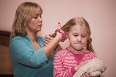 A women brushes a young girl's hair who has a determined look on her face, possibly reflecting on a bad memory.