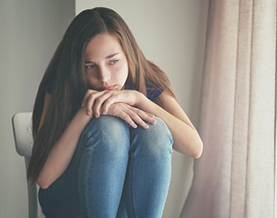 A female teen sits with chin to knees looking solemn.