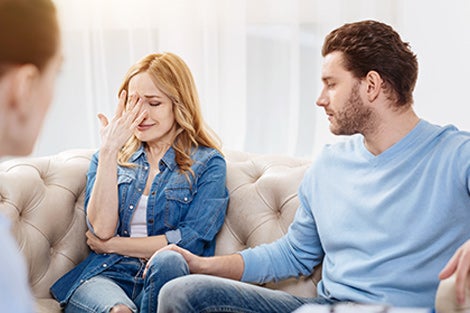 A young woman cries while her spouse looks on comforting.