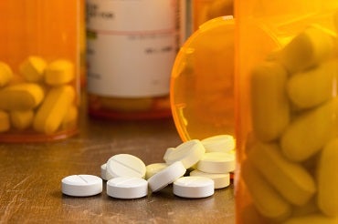 A prescription pill bottle has been tipped over with round white pills spilling out onto a table.