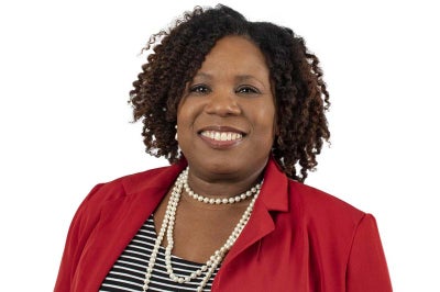African American woman in red jacket and pearls smiles for the camera.