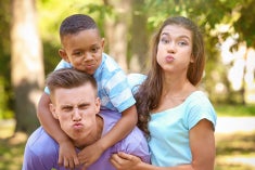 A young caucasian couple, makes funny faces with a young African American boy about 10 years old, being silly.