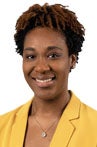 Young African American woman smiling at the camera wearing a bright yellow blazer.
