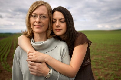 A brown-haired young woman embraces an older woman with light hair.
