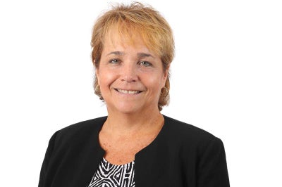 Woman with short blonde hair wears a black professional jacket with stripe shirt.