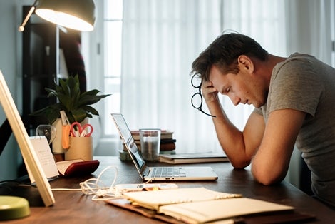 Man in front of laptop on desk holding glasses in hand looking tired.