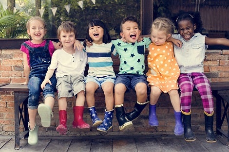 A diverse group of young kids around the age of 7 laughing with each other while sitting on a bench.