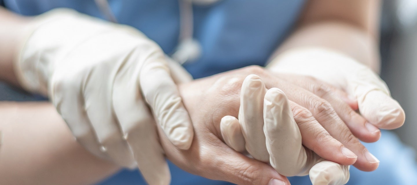 Nurse with gloved hands holding patient's hand