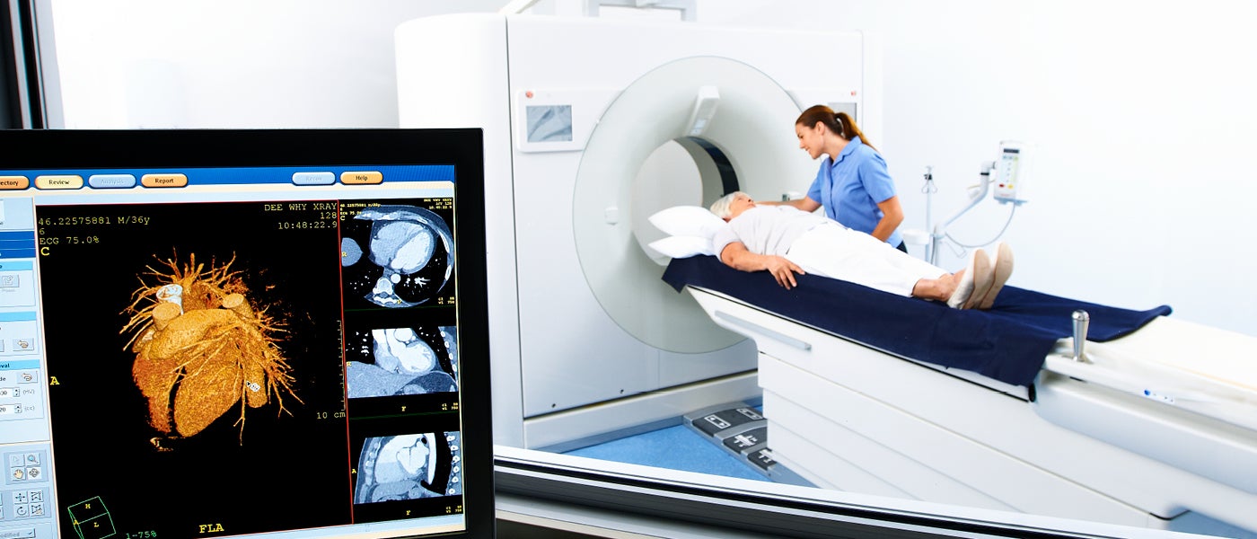 A technician talking to a patient laying on a CT machine bed