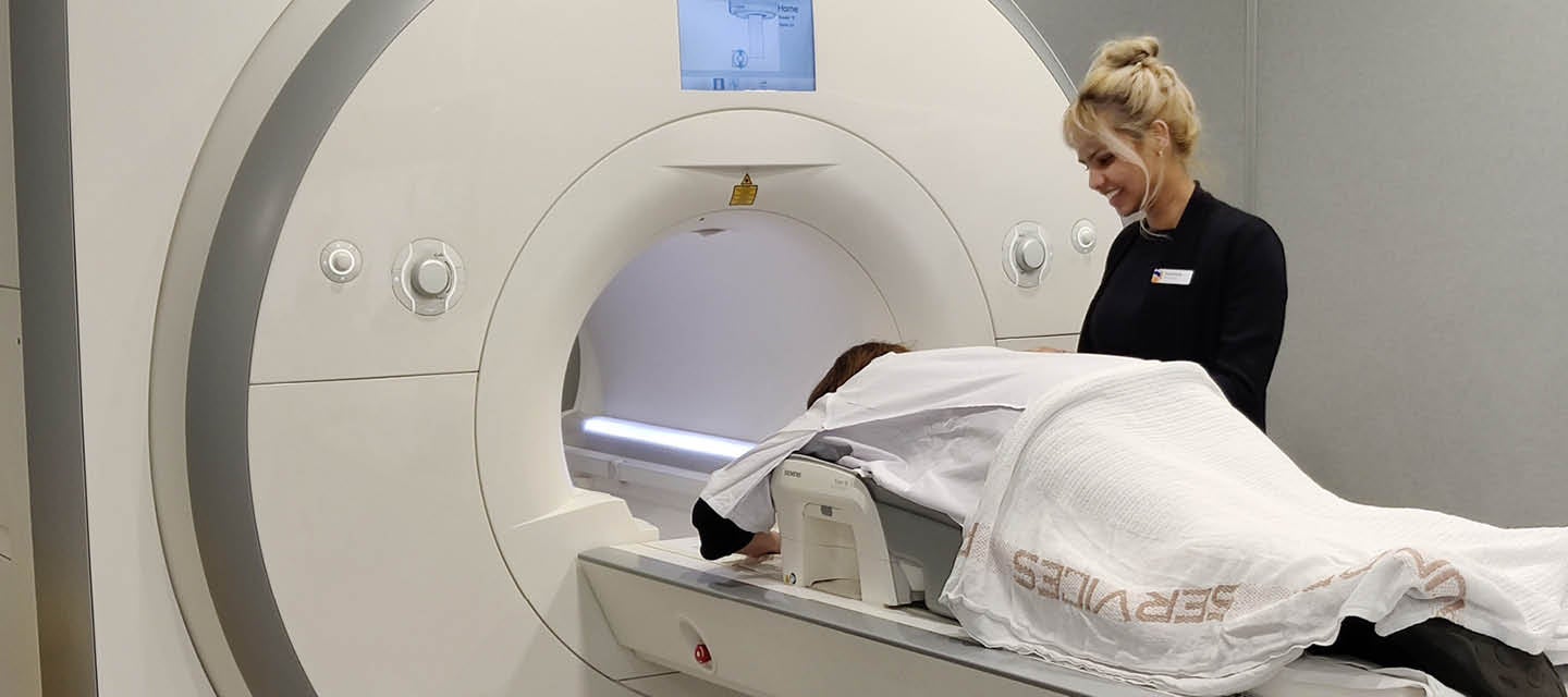 Patient laying down flat on MRI bed and technician standing over with a smile