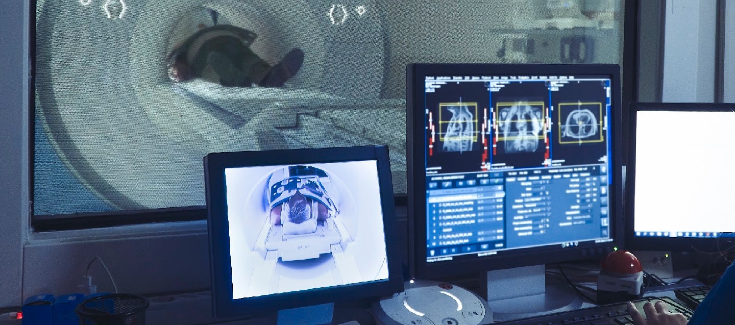 Man having an MRI scan seen through the glass with screens in the foreground