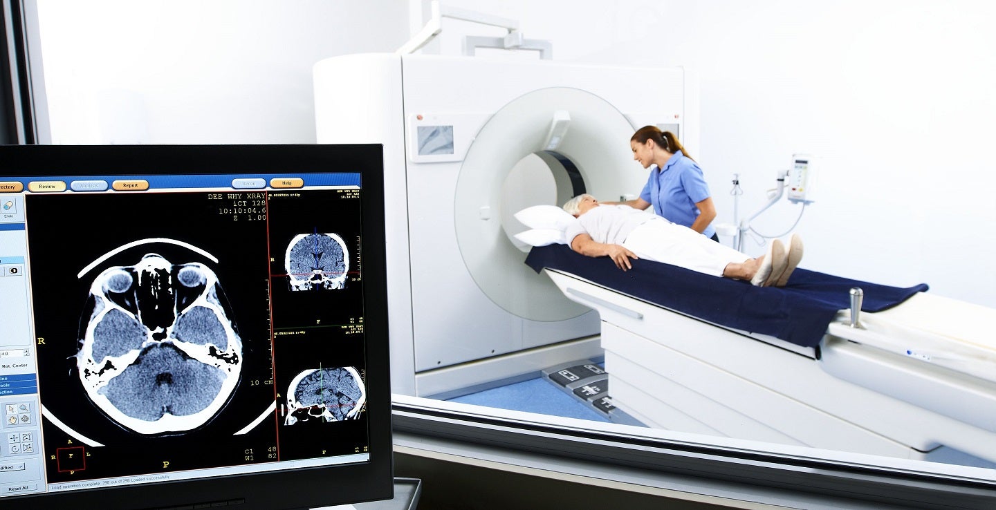 Patient and technician with CT machine and scan of brain on screen