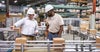 Two men in hardhats talking while surrounded by conveyors handling cardboard boxes