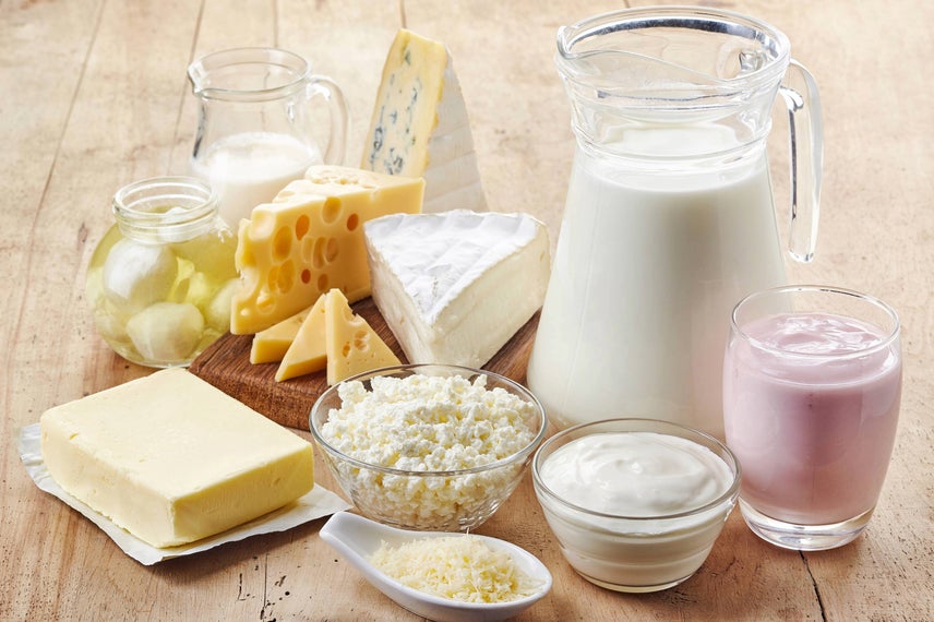 Verschiedene Molkereilebensmittel und -getränke auf einem Holztisch. Dazu gehören Käse, Joghurt, Butter und Milch.