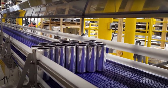 Sistema de banda transportadora industrial que transporta latas de aluminio para bebidas a través de una línea de producción automatizada en unas modernas instalaciones de fabricación.